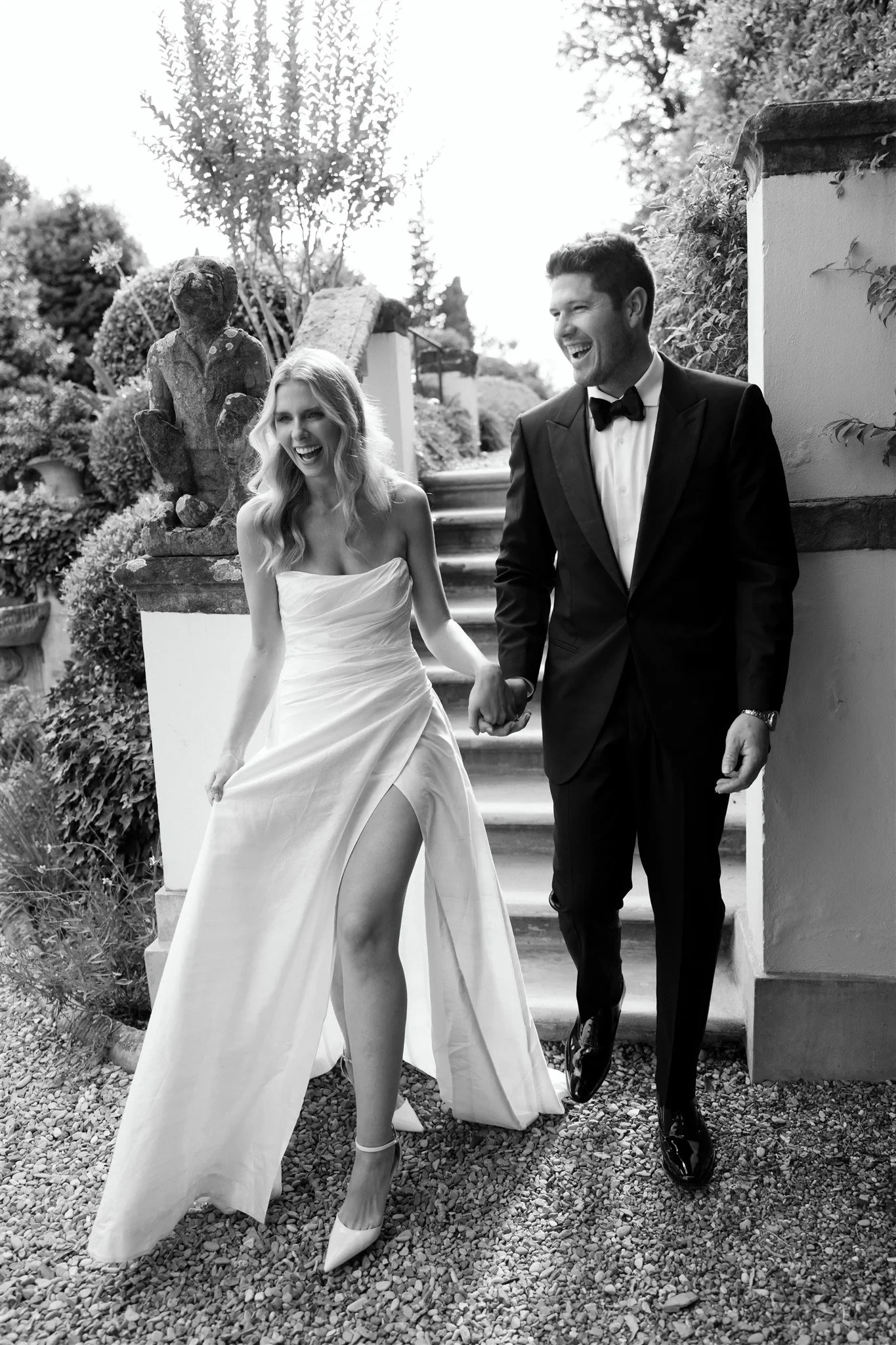 Black-and-white photograph of Holly and Matt walking hand in hand along a garden path, at Belmond Villa San Michele in Fiesole, overlooking Florence, Tuscany, Italy, for an Elopement Collective elopement. Photo by Khara from House of Lucie.