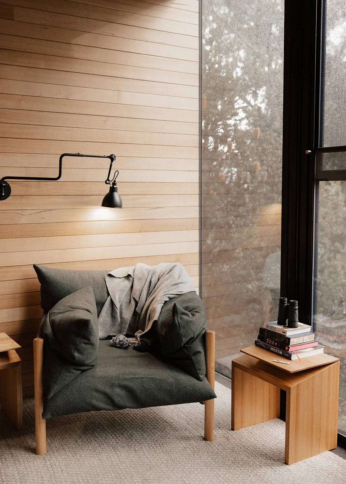 A green armchair and timber side table beside tall windows and a pale timber wall, at Pumphouse Point, Lake St Clair, Tasmania, for an Elopement Collective elopement. Photo by Bulb Creative.