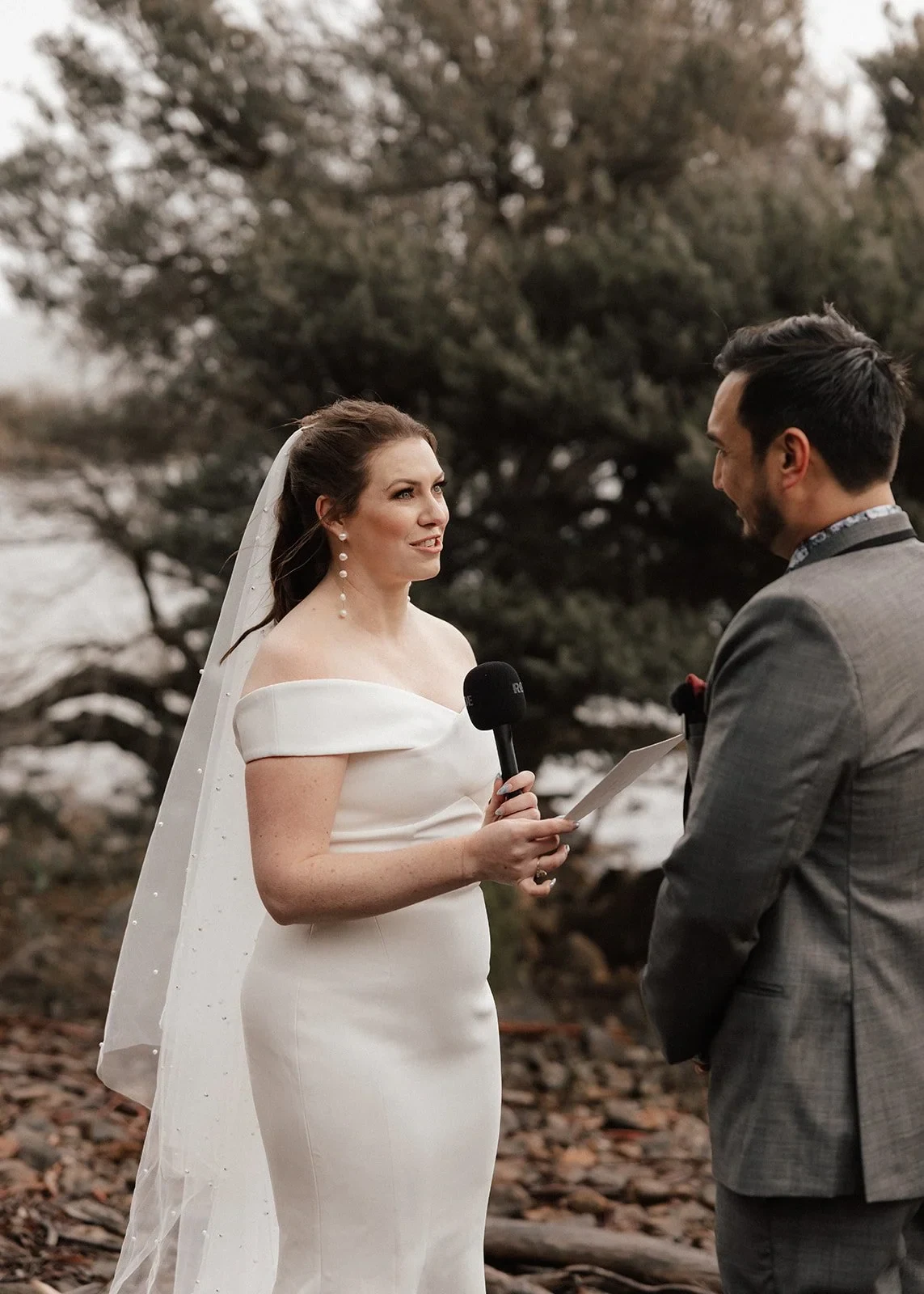Sarah reading her vows to Jono on the rocky lakeshore, at Pumphouse Point, Lake St Clair, Tasmania, for an Elopement Collective elopement. Photo by Bulb Creative.