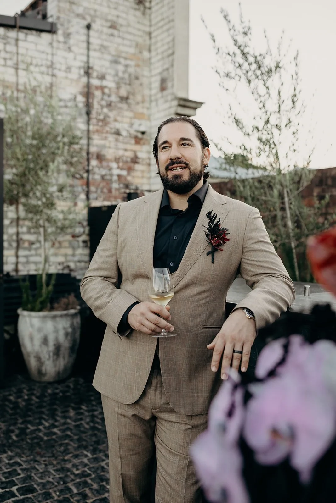 Daniel leaning on the rooftop railing with a glass of sparkling wine, at Agnes Restaurant in Fortitude Valley, Brisbane, for an Elopement Collective elopement. Photo by Tessa Shannon.